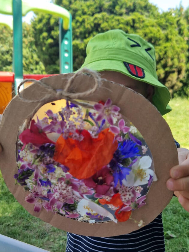 Дитина показує аплікацію з квітів у саду дитячого садка Mariposa